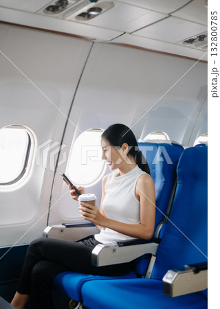Attractive Asian female passenger of airplane sitting in comfortable seat while working laptop and tablet. Travel in style, work with grace. 132800785