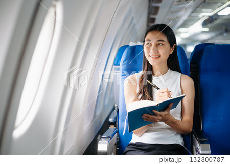 Attractive Asian female passenger of airplane sitting in comfortable seat while working laptop and tablet. Travel in style, work with grace. Attractive Asian female passenger of airplane sitting in comfortable seat while working laptop and tablet. Travel in style, work with grace. 132800787