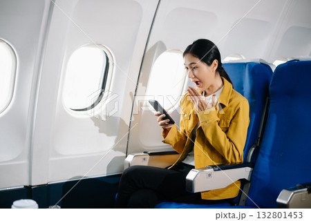 Attractive Asian female passenger of airplane sitting in comfortable seat while working laptop and tablet. Travel in style, work with grace. 132801453