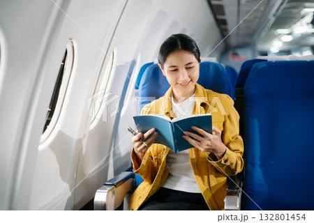Attractive Asian female passenger of airplane sitting in comfortable seat while working laptop and tablet. Travel in style, work with grace. Attractive Asian female passenger of airplane sitting in comfortable seat while working laptop and tablet. Travel in style, work with grace. 132801454
