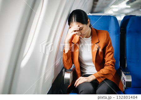 frustrated woman sitting on an airplane with her head in her hands. Asian woman sitting in a seat in airplane frustrated woman sitting on an airplane with her head in her hands. Asian woman sitting in a seat in airplane 132801484