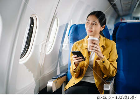 Attractive Asian female passenger of airplane sitting in comfortable seat while working laptop and tablet. Travel in style, work with grace. 132801607