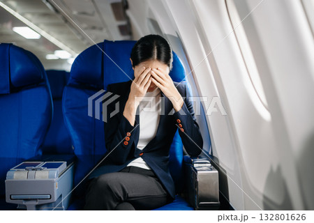 frustrated woman sitting on an airplane with her head in her hands. Asian woman sitting in a seat in airplane frustrated woman sitting on an airplane with her head in her hands. Asian woman sitting in a seat in airplane 132801626