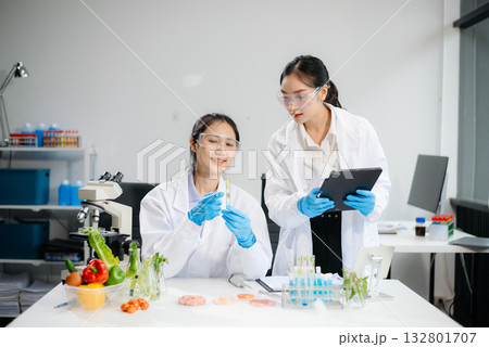 Two Asian scientists in a lab conducting food research using a microscope and lab equipment, showcasing innovation in food science Two Asian scientists in a lab conducting food research using a microscope and lab equipment, showcasing innovation in food science 132801707