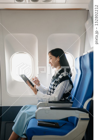 Attractive Asian female passenger of airplane sitting in comfortable seat while working laptop and tablet with mock up area using wireless connection. Attractive Asian female passenger of airplane sitting in comfortable seat while working laptop and tablet with mock up area using wireless connection. 132802212