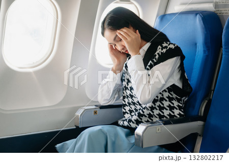 Photo of a frustrated woman sitting on an airplane with her head in her hands. woman sitting in a seat in airplane Photo of a frustrated woman sitting on an airplane with her head in her hands. woman sitting in a seat in airplane 132802217