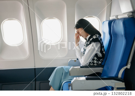 Photo of a frustrated woman sitting on an airplane with her head in her hands. woman sitting in a seat in airplane 132802218