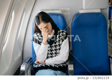 Photo of a frustrated woman sitting on an airplane with her head in her hands. woman sitting in a seat in airplane 132802219