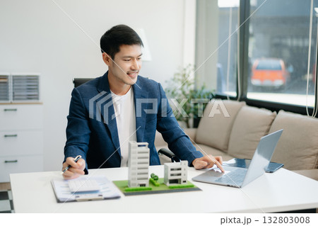 Young real estate agent worker working with laptop and tablet at table in office and small house 132803008