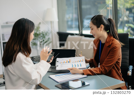 Businesswomen work and discuss their business plans. A Human employee explains and shows her colleague the results paper Businesswomen work and discuss their business plans. A Human employee explains and shows her colleague the results paper 132803270