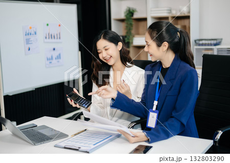 Businesswomen work and discuss their business plans. A Human employee explains and shows her colleague the results paper 132803290