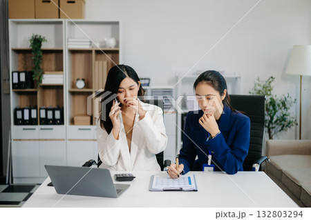 Female discussing new project with Female colleague. Young women talking with young Asian man in office. 132803294