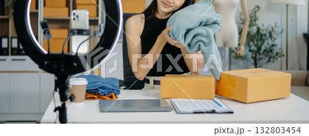 Asian lady blogger showing clothes in front of the camera to recording vlog video live streaming at her shop. Asian lady blogger showing clothes in front of the camera to recording vlog video live streaming at her shop. 132803454