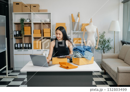 Asian lady blogger showing clothes in front of the camera to recording vlog video live streaming at her shop.  132803499