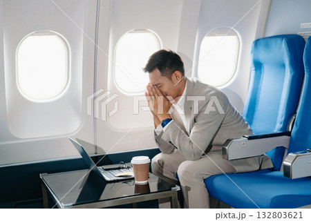 Photo of a frustrated man sitting on an airplane with her head in her hands. Asian Businessman sitting 132803621
