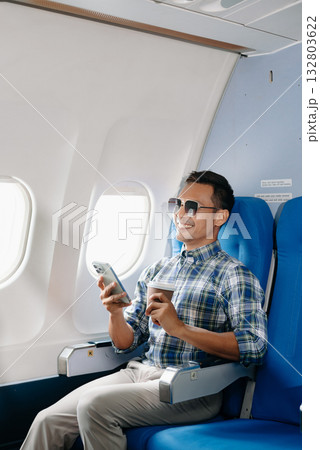 Asian male passenger of airplane sitting in comfortable seat while working laptop and tablet with mock up area using wireless connection. Travel in style, 132803622