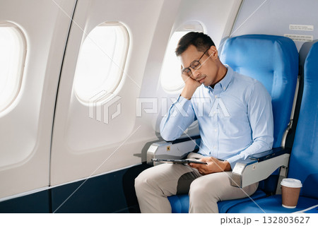 Asian male passenger of airplane sitting in comfortable seat while working laptop and tablet with mock up area using wireless connection. Travel in style, Asian male passenger of airplane sitting in comfortable seat while working laptop and tablet with mock up area using wireless connection. Travel in style, 132803627