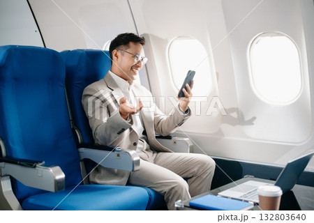 Young Asian executive excels in first class, multitasking with digital tablet, laptop and smartphone. Travel in style, 132803640