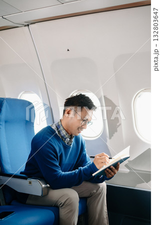 Asian male passenger of airplane sitting in comfortable seat while working laptop and tablet with mock up area using wireless connection. Travel in style, 132803647