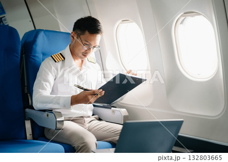Asian Confident male pilot in uniform leaning at the passenger seat while standing inside of the airplane flight cockpit during takeoff 132803665
