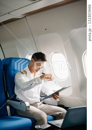 Asian Confident male pilot in uniform leaning at the passenger seat while standing inside of the airplane flight cockpit during takeof 132803666