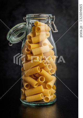 Uncooked rigatoni pasta in jar on black table. 132804665