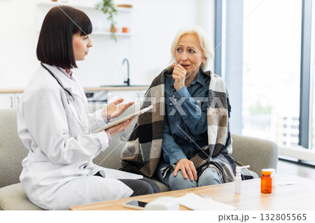 A female doctor is consulting with an elderly woman who appears to be sick, possibly at her home, offering medical advice. A female doctor is consulting with an elderly woman who appears to be sick, possibly at her home, offering medical advice. 132805565