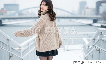 雪の川沿いの階段で振り返り微笑むニットの女性 132806578
