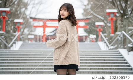 雪の神社で振り返り微笑むニットとスカートの女性 132806579