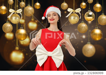 Woman in festive attire posing with a bow surrounded by ornaments Woman in festive attire posing with a bow surrounded by ornaments 132806999