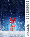 Christmas card with a toy ball and a gift inside on the snow. Festive banner with hoarfrost on night abstract defocused lights background. 132808661