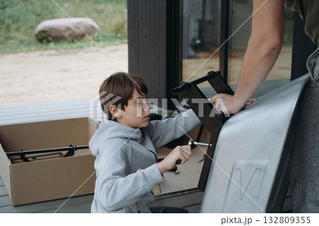 teenage boy assemble a wheelbarrow with a screwdriver, father assists 132809355