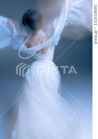 White gown and pearls swirling in soft blur, arms raised in ethereal light 132810693