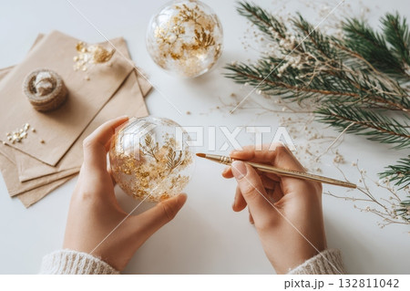 Woman painting white snowflake design on Christmas bauble for cozy holiday home decor. 132811042