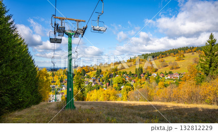 Visitors can enjoy stunning autumn colors at Bukova Hora in Cenkovice. The scenic chairlift overlooks vibrant trees and a quaint village surrounded by mountains. 132812229