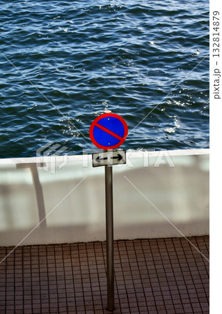 Road sign, no parking sign in the waterfront with the sea in the background. Calm seascape. City scene and nature scene. Road sign, no parking sign in the waterfront with the sea in the background. Calm seascape. City scene and nature scene. 132814879
