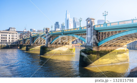 Bright sunlight reflects off the Thames River as Southwalk Bridge stands proudly in London. The bridge connects the bustling cityscape with scenic views along the riverbank. Bright sunlight reflects off the Thames River as Southwalk Bridge stands proudly in London. The bridge connects the bustling cityscape with scenic views along the riverbank. 132815798