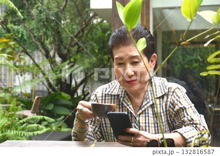 elder woman enjoy to drinking coffee read book and used mobile phone in cafe garden on afternoon elder woman enjoy to drinking coffee read book and used mobile phone in cafe garden on afternoon 132816587