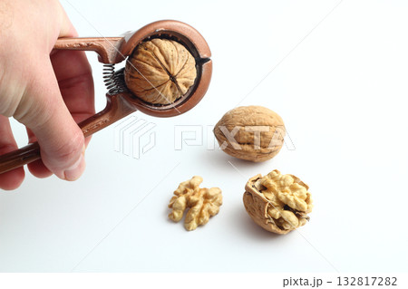 Nutcracker held in male hand and crack a walnut isolated on a white background. Nutcracker held in male hand and crack a walnut isolated on a white background. 132817282