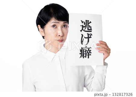 逃げ癖と書かれた紙を持ち口をとがらせるシニア女性 132817326