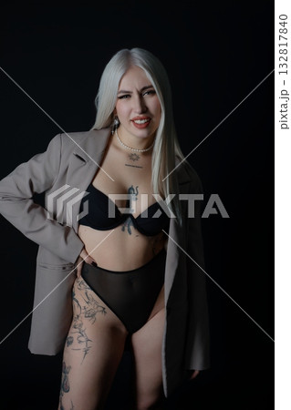 Confident model in a stylish blazer and lingerie wearing bold tattoos indoors 132817840