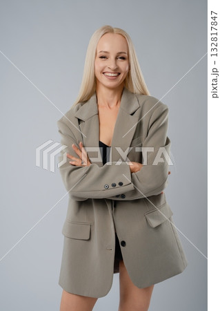 Confident woman in oversized blazer poses in studio against gray backdrop 132817847