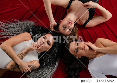 Three women pose elegantly on a red backdrop in stylish lingerie Three women pose elegantly on a red backdrop in stylish lingerie 132817892