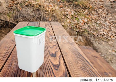 white container with a green lid on a wooden table in nature 132818870