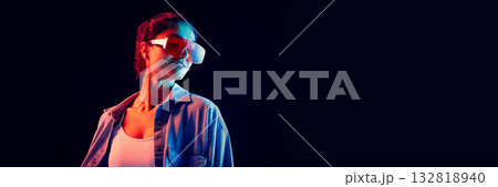 Stylish woman with red visor glasses posing under neon light expressing confidence. Banner 132818940