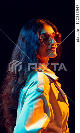 Stylish woman in glasses posing in colorful light expressing self-assured elegance 132818947