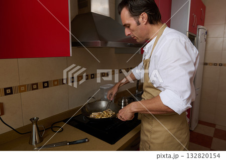 Man Cooking In Kitchen With Apron At Stove, Preparing Food In Wok, Home Cooking Scene 132820154