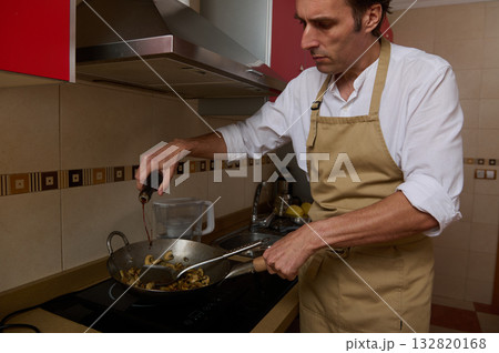 Busy Chef Man Cooking Mushrooms in Pan in Modern Kitchen, Apron On, Pouring Oil 132820168