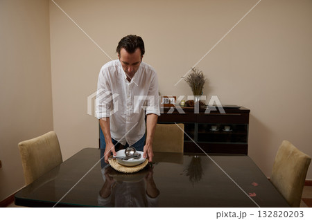 Man In White Shirt Sets Dinner Table In Minimal Dining Room 132820203