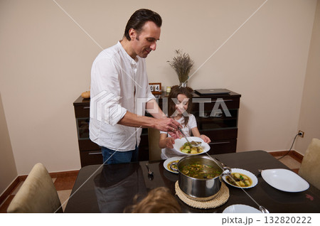 Father Cooking Soup And Serving Dinner While Daughter Helps In The Kitchen Father Cooking Soup And Serving Dinner While Daughter Helps In The Kitchen 132820222